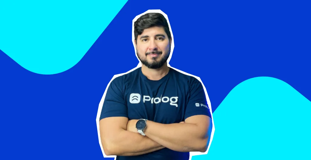 Foto do Tiago Damazio de braços cruzados. Atrás, fundo azul com turquesa.